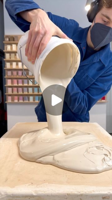 a man in blue shirt pouring white paint on a piece of wood with headphones