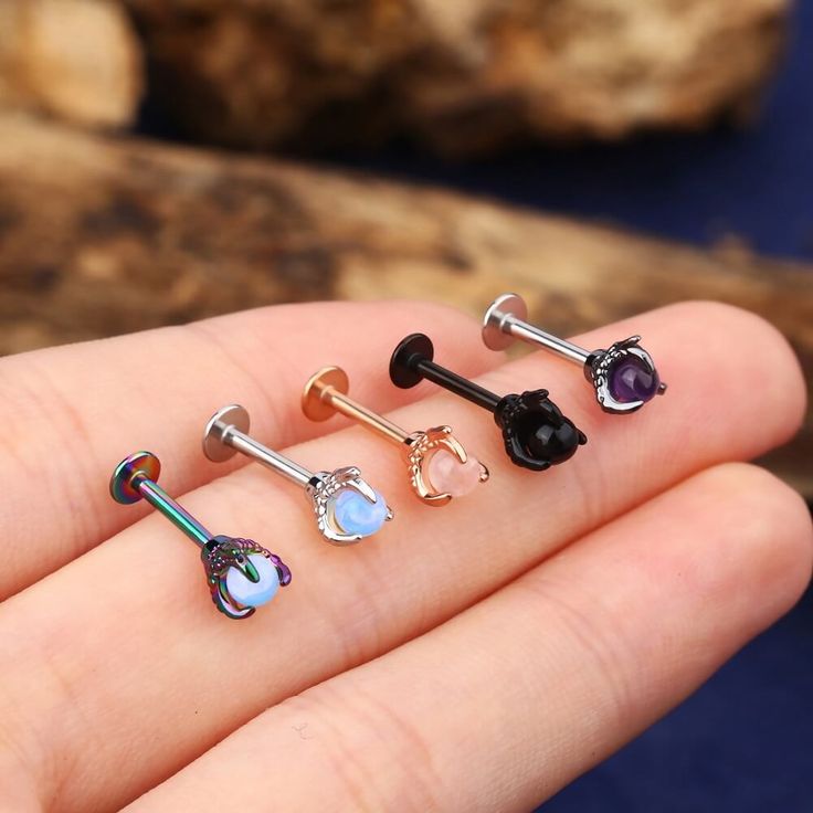 four different colored nose piercings on someone's finger in front of a rock