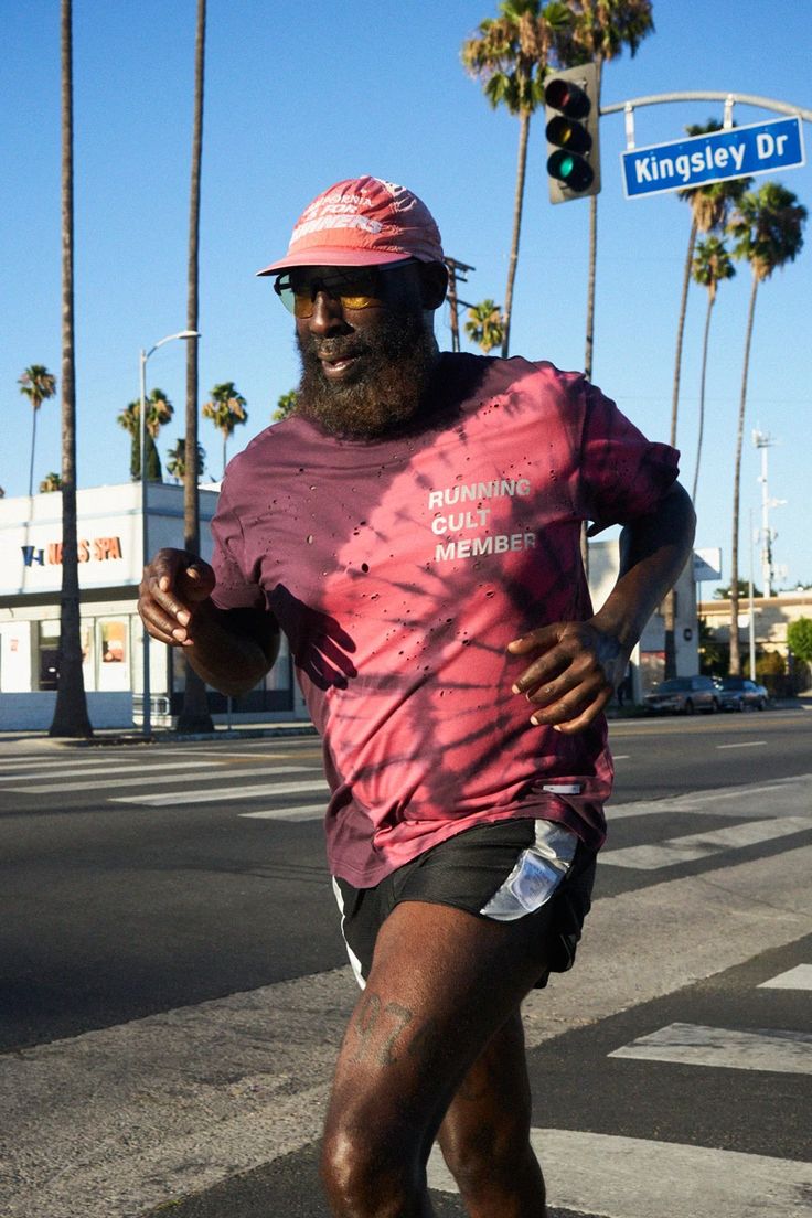 a man in pink shirt and black shorts running on street with palm trees behind him