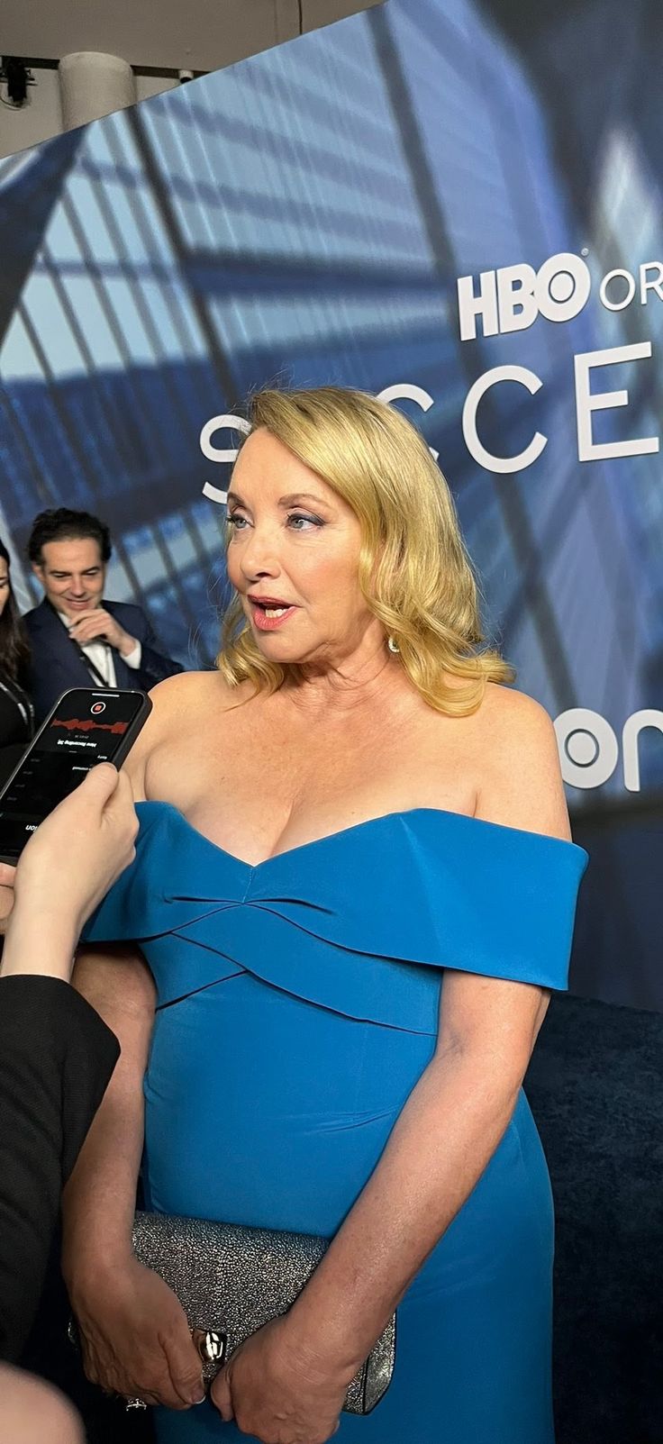 a woman in a blue dress talking to someone on the red carpet at an event