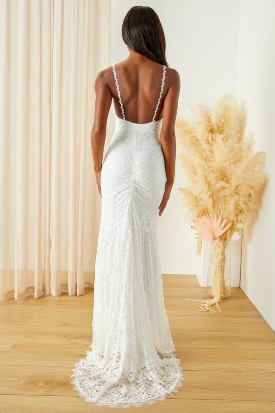 the back of a woman in a white wedding dress standing next to a tall plant