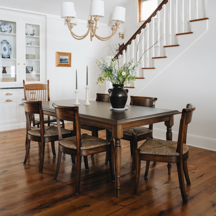 a dining room table with chairs and a vase on top of it in front of the stairs