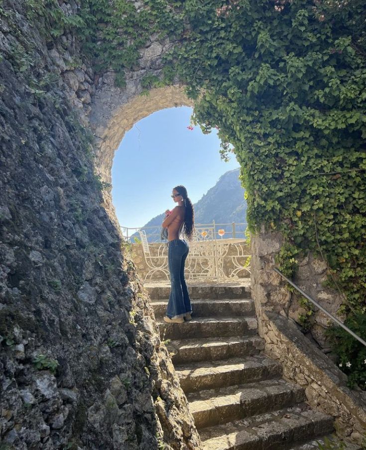 a woman is standing on some steps in front of an arch that leads to the ocean