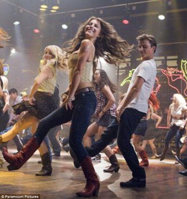 a group of young people dancing on stage with lights in the background and one person holding a microphone