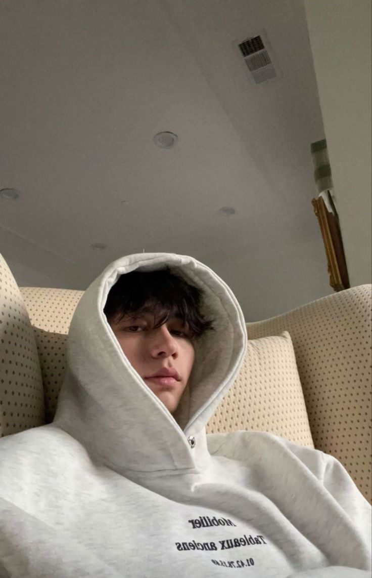 a young man is wrapped up in a white hoodie while sitting on a couch