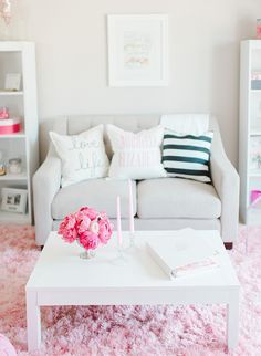 a white coffee table with pink flowers on it in front of a gray couch and bookshelf