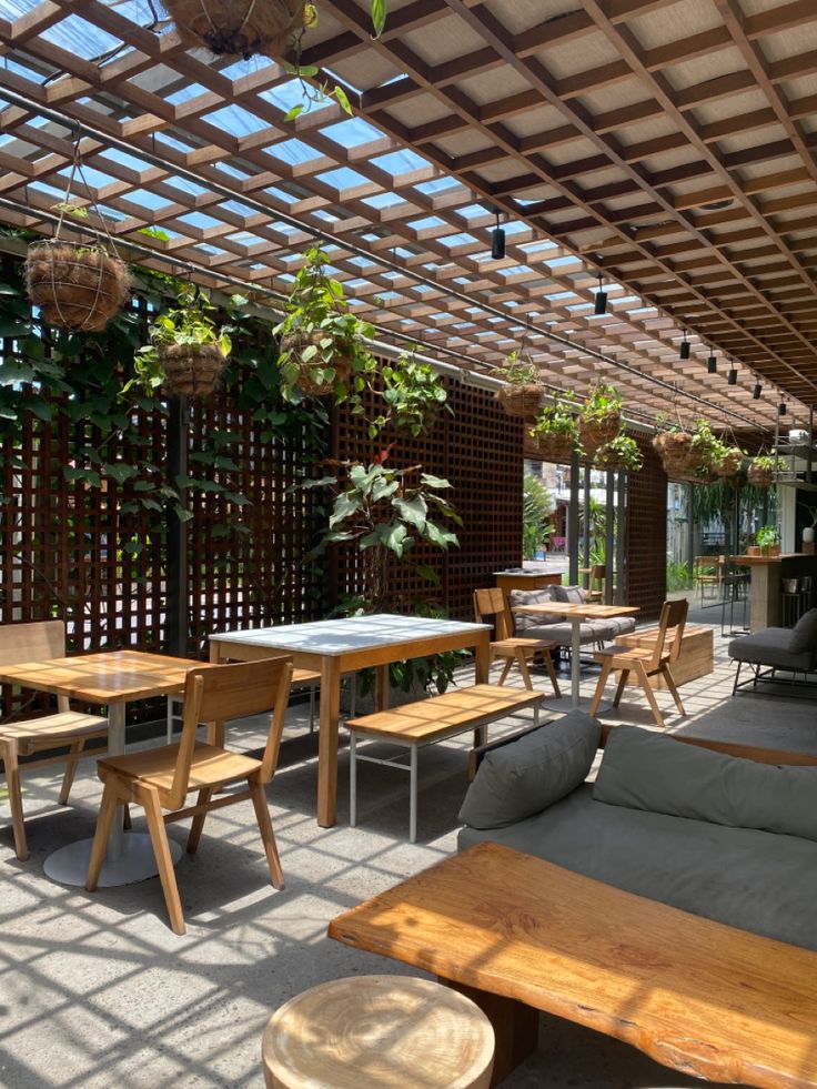 an outdoor seating area with wooden tables and couches under a pergolated roof