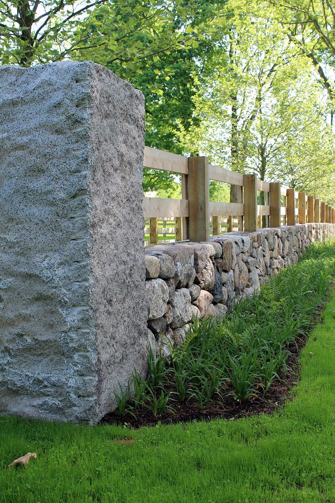 a stone wall in the grass next to a wooden fence