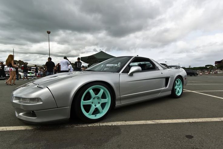 a silver sports car with blue rims parked in a parking lot next to other cars