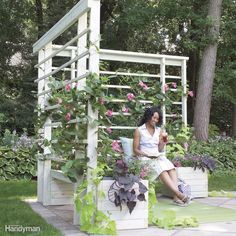 a woman sitting on a bench next to a garden trellis with pink flowers in it