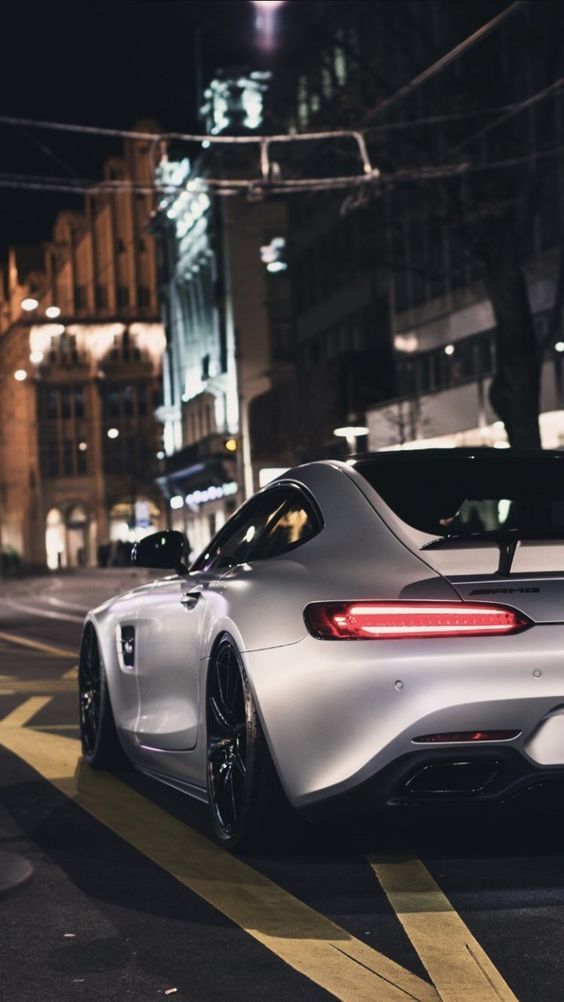 a white sports car is parked on the side of the road at night in front of some buildings