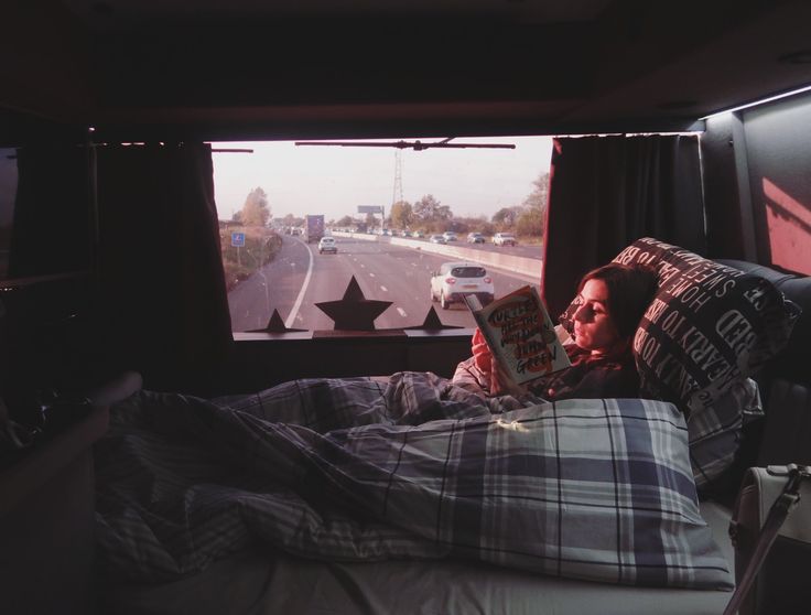 a woman laying in bed reading a book while looking out the window at an interstate highway