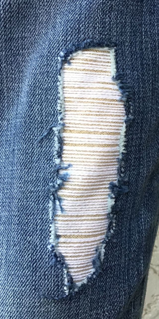 the back pocket of a pair of blue jeans with ripped edges and white stitching