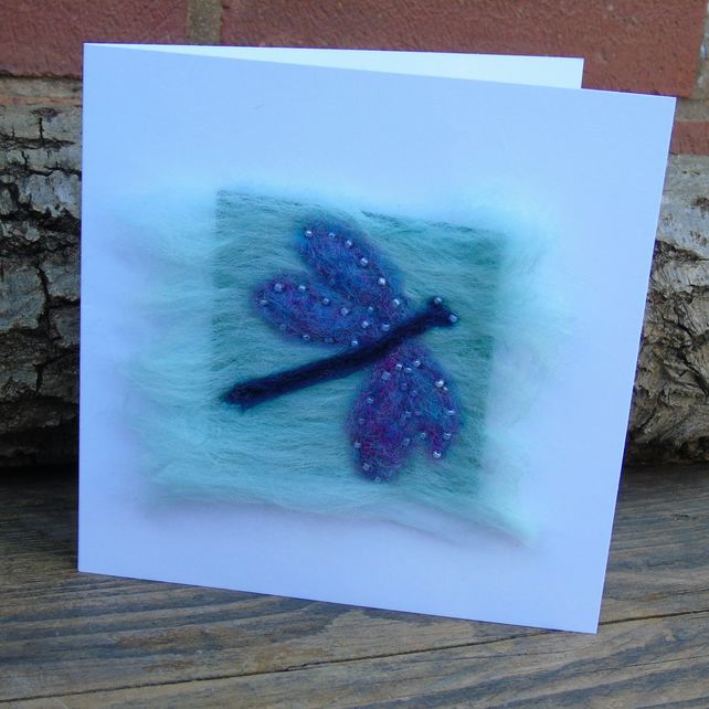 a card with a blue dragonfly on it sitting next to a piece of wood