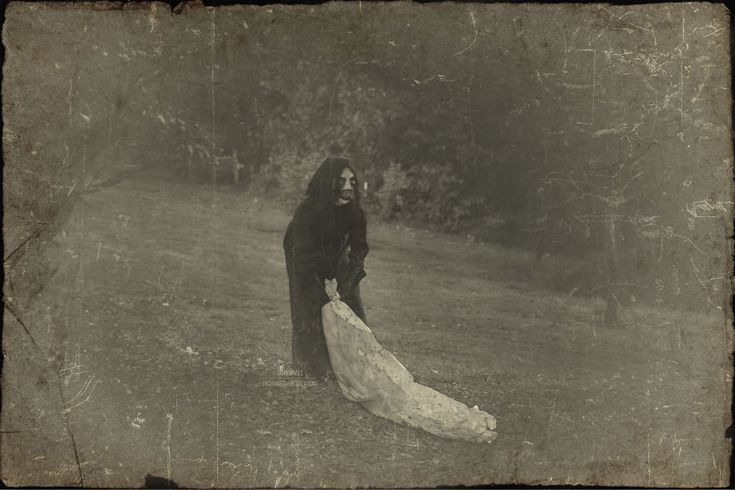 an old black and white photo of a woman in a long dress standing in the grass