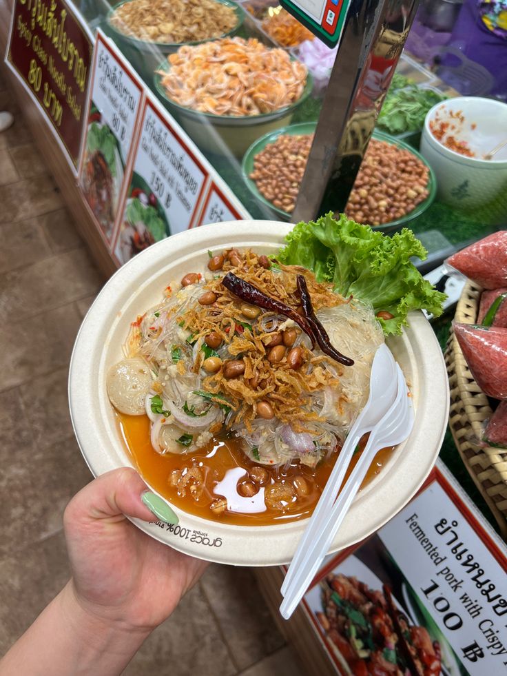 a person holding a paper plate with food on it in front of a display case