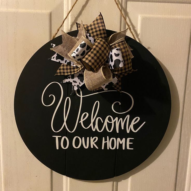 a welcome to our home sign hanging on a door with burlocks and bows