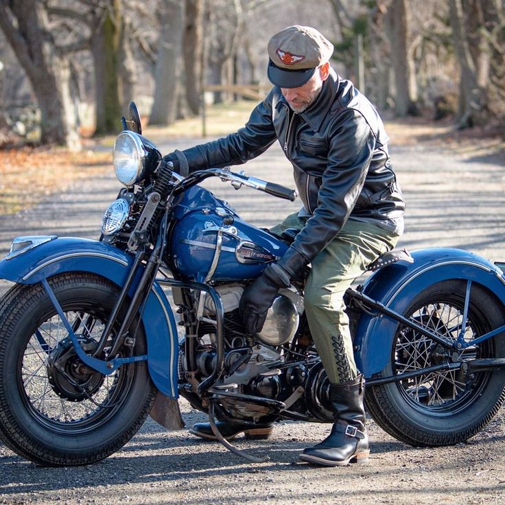 a man sitting on top of a blue motorcycle in the middle of a road next to trees