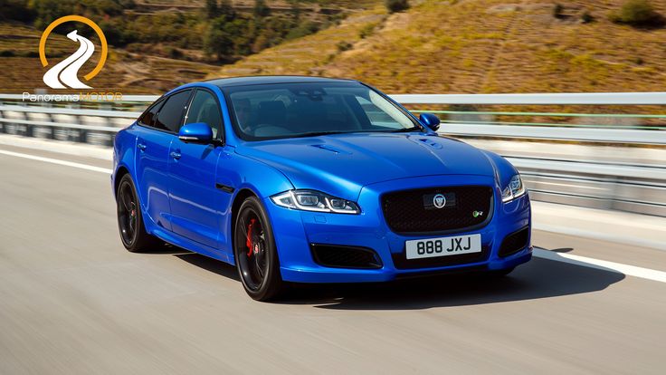 a blue car driving down the road with mountains in the backgrouund and hills in the background