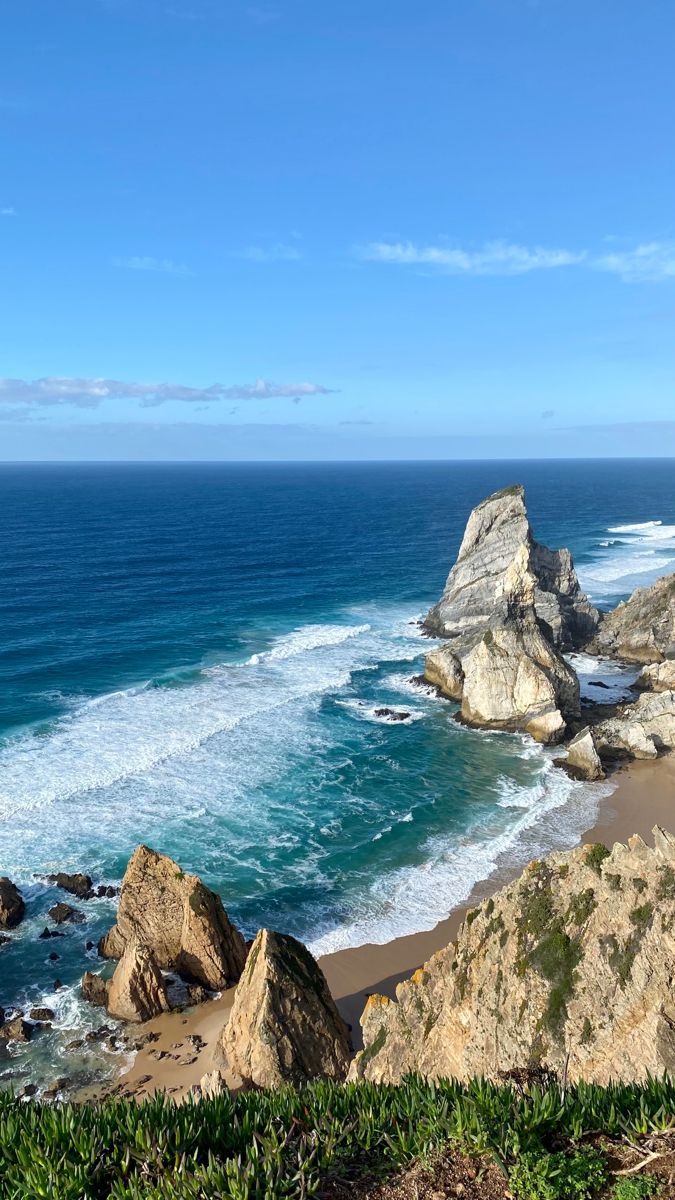 an ocean view from the top of a hill with waves crashing on it and rocks in the foreground