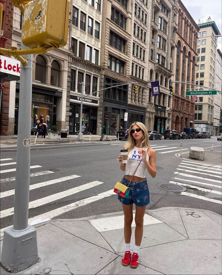 a woman is standing on the sidewalk drinking coffee