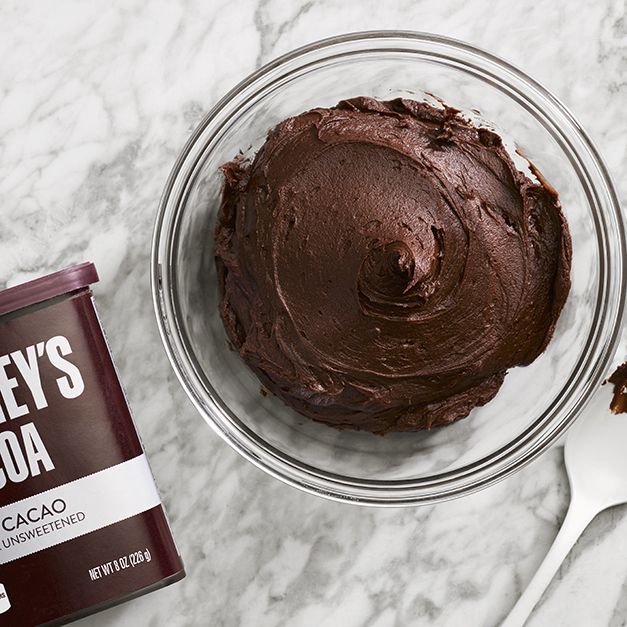 a bowl of chocolate frosting next to a container of ice cream on a marble counter