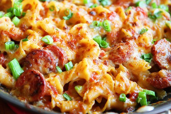 a skillet filled with pasta and meat covered in cheese, green onions and sauce