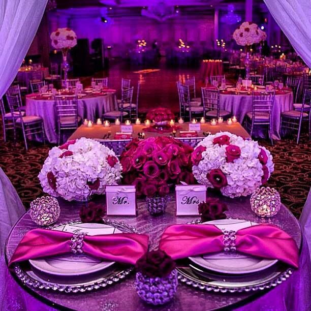 the table is set with purple and white flowers, silverware, and place settings