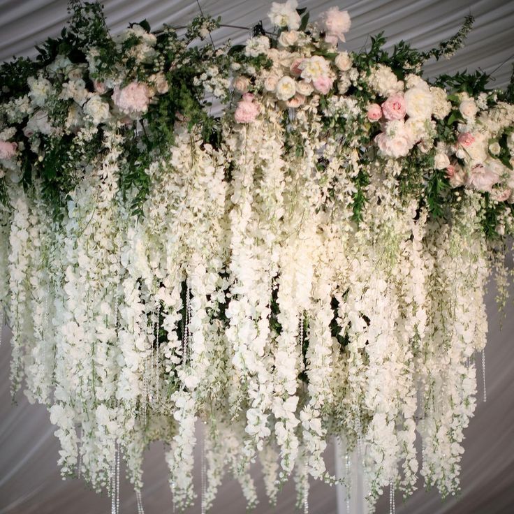 an arrangement of white flowers and greenery hanging from the ceiling at a wedding reception