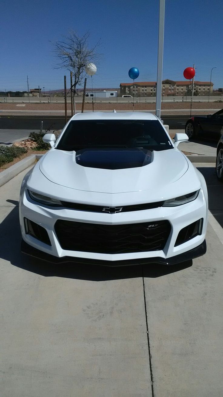 a white chevrolet camaro parked in front of a gas station with balloons attached to it