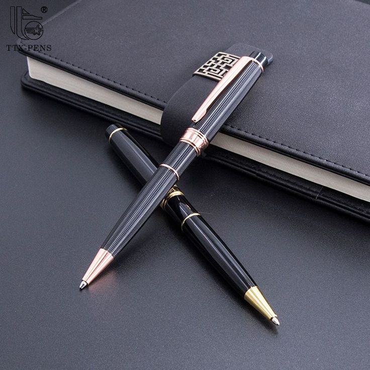 a pen sitting on top of an open book next to a black notebook with gold trim