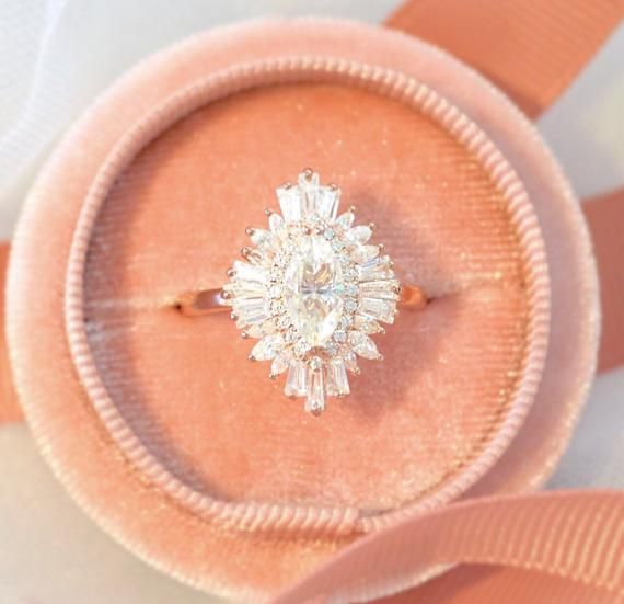 an engagement ring is sitting on top of a pink velvet box with a ribbon around it