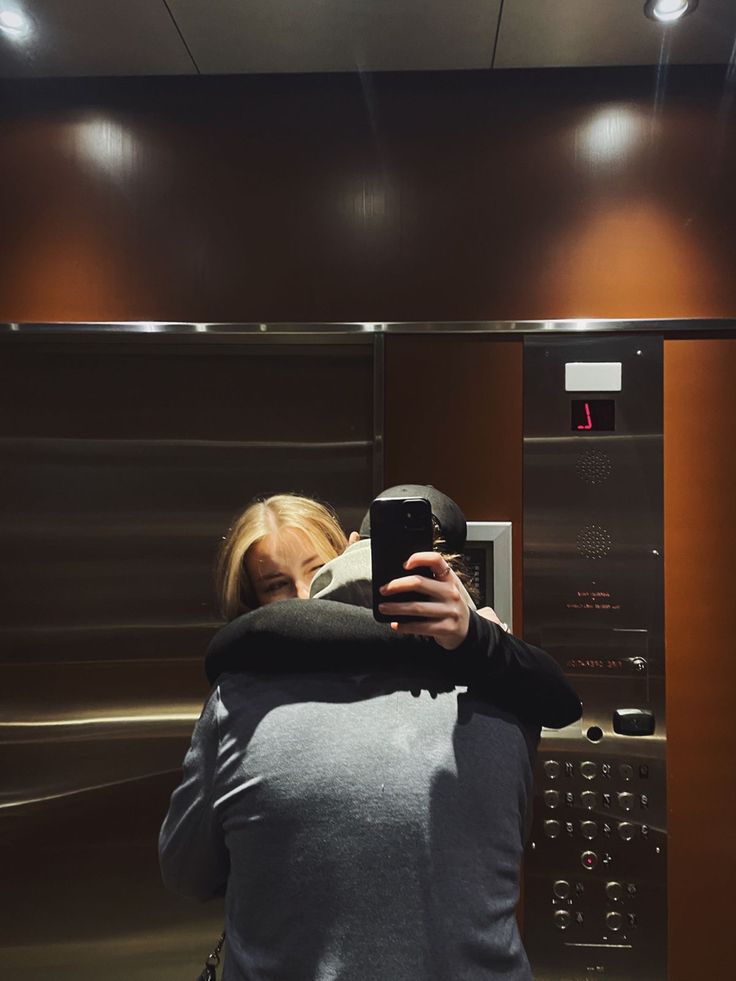 a woman taking a selfie with her cell phone in front of an elevator door