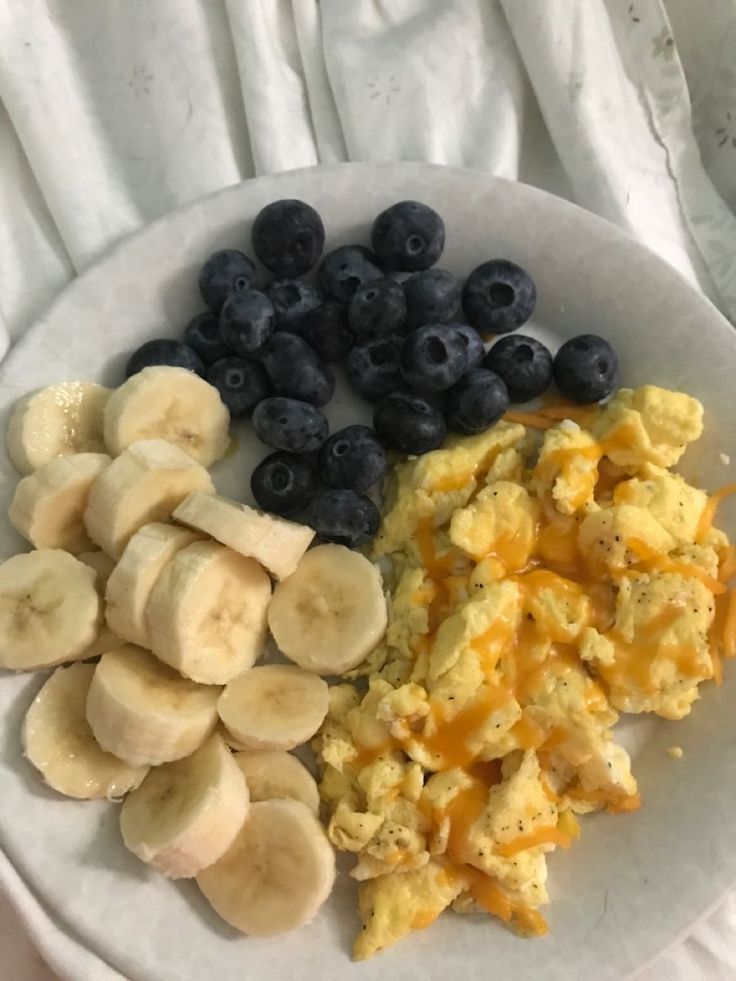 the breakfast plate has bananas, blueberries, and scrambled eggs on it with yogurt