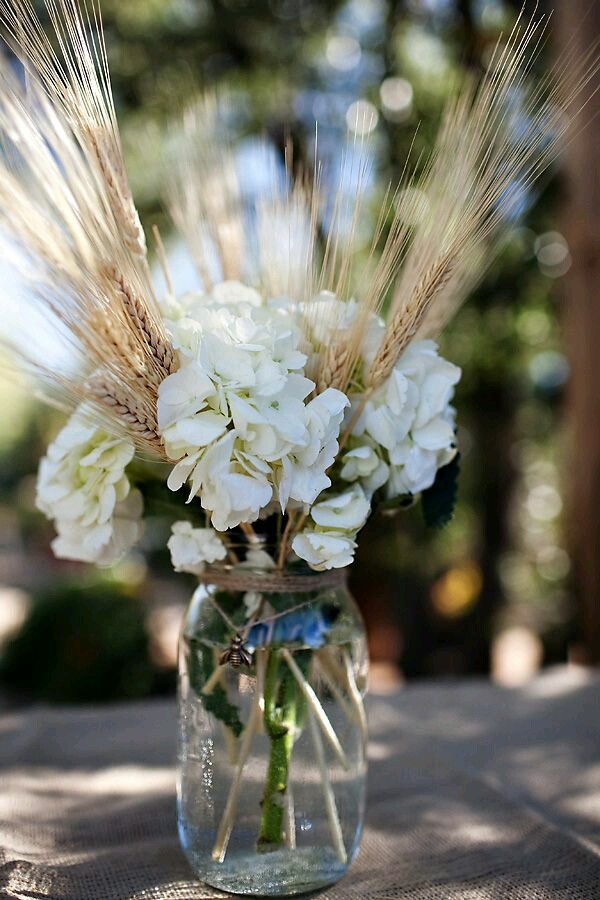 a vase filled with white flowers sitting on top of a wooden table covered in grass