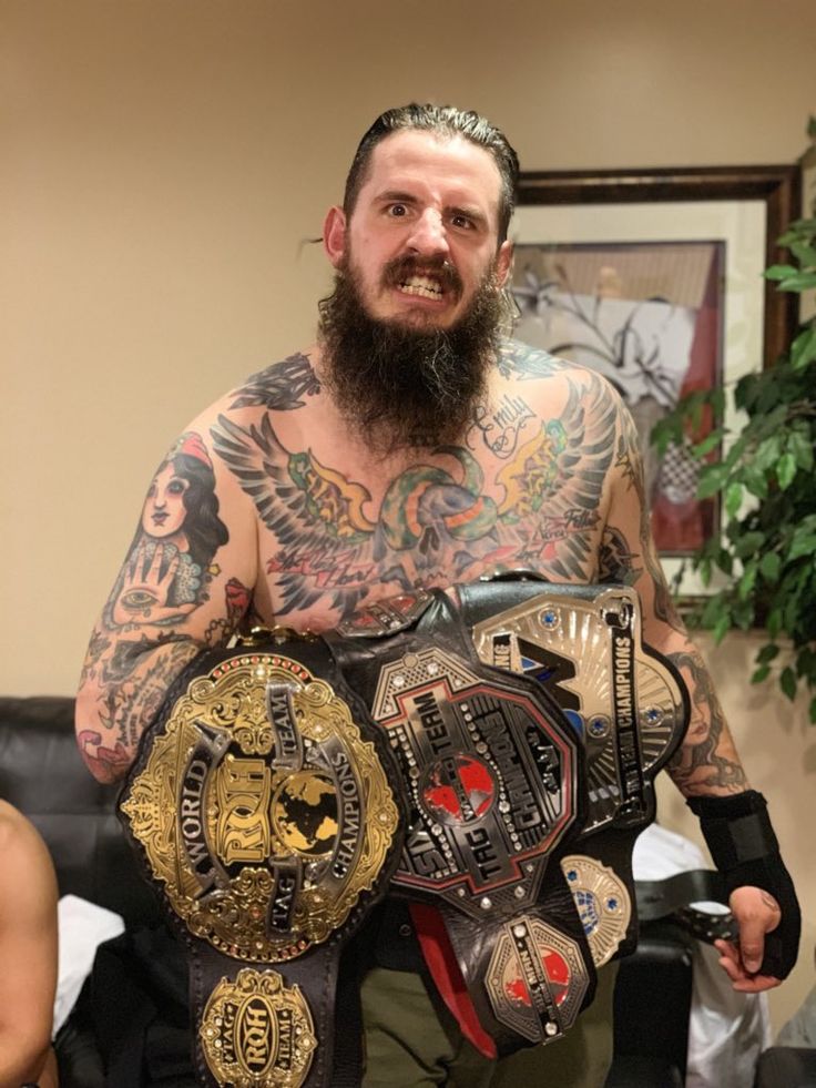 a bearded man with tattoos holding two belts