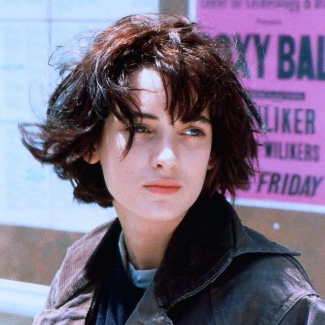 a woman with short hair standing in front of a sign and looking at the camera