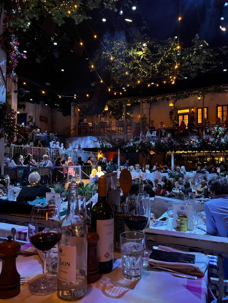 a table with wine bottles and glasses on it at a restaurant or bar in the evening