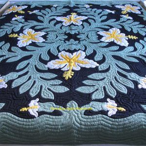 a blue and yellow quilt on a bed with white flowers in the center, along with an intricately designed border