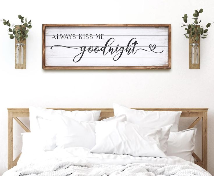 a bed with white sheets and pillows in front of a wooden sign that says always kiss me goodnight