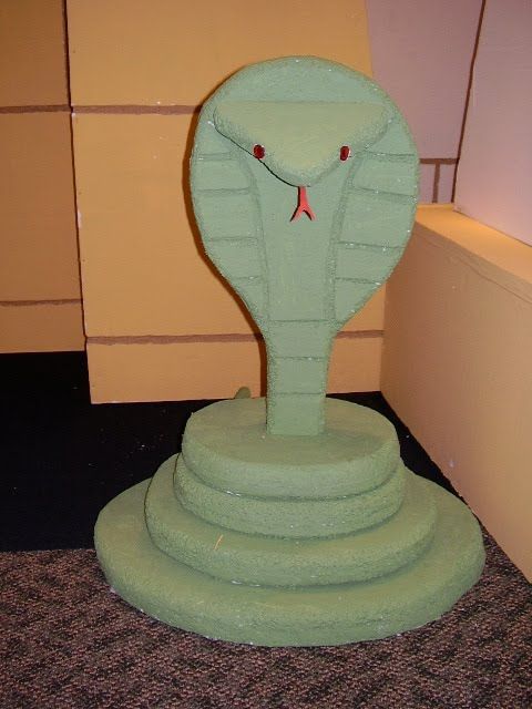 a green snake statue sitting on top of a carpeted floor next to a wall