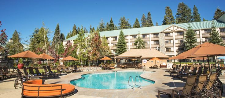 an outdoor swimming pool surrounded by lounge chairs and umbrellas in front of a hotel