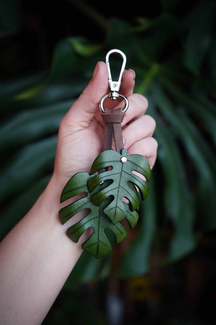 a person holding a green leaf shaped keychain in front of a palm tree