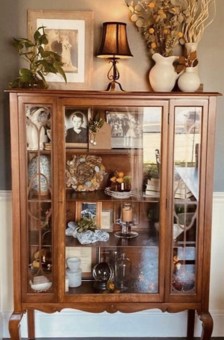 a wooden cabinet with glass doors and pictures on it's front door, next to a lamp