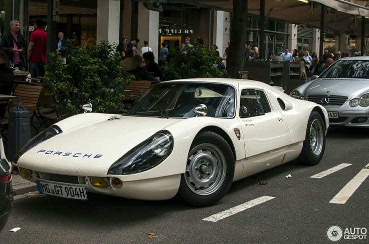 a white sports car is parked on the side of the road in front of other cars