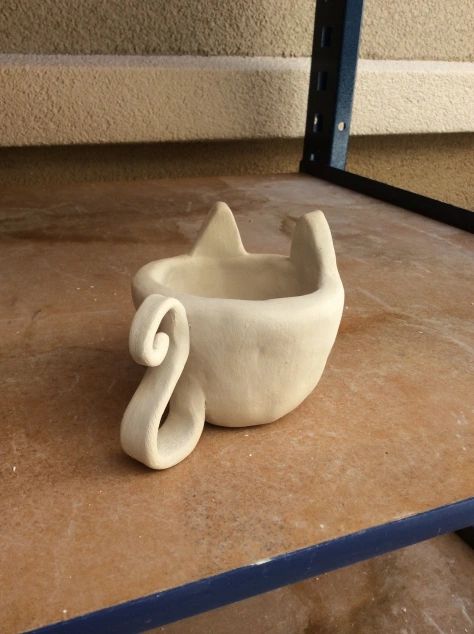 a white cat shaped bowl sitting on top of a counter next to a metal shelf