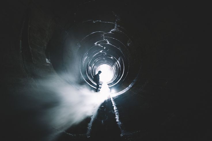 a man standing in the middle of a dark tunnel with light coming from behind him