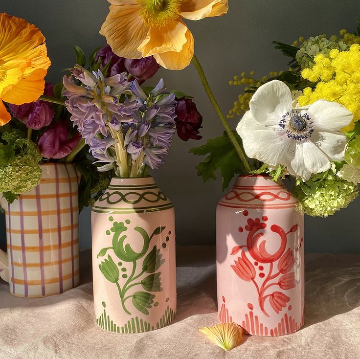 three vases filled with different types of flowers on a cloth covered tableclothed surface