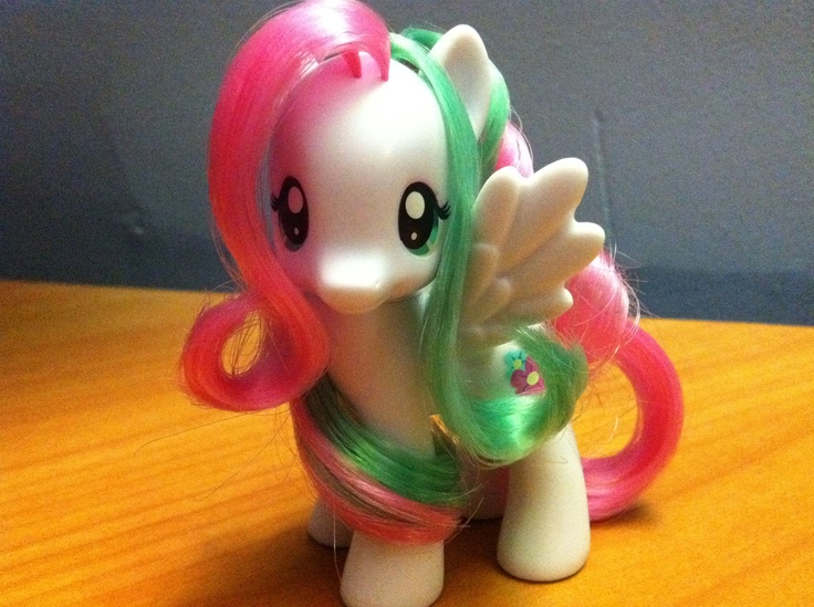 a toy pony with pink, green and white manes sitting on top of a wooden table