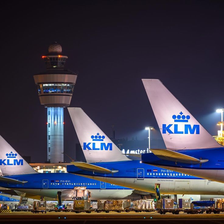 three blue and white jetliners sitting on top of an airport tarmac at night